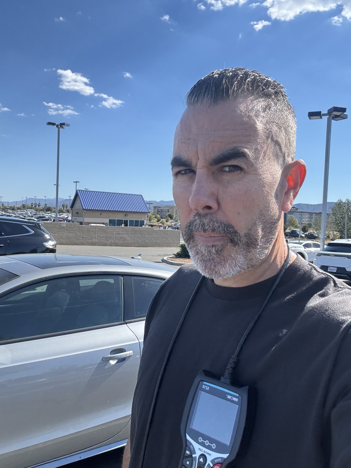 Brian Moreno outdoors beside a car, holding a diagnostic scanner